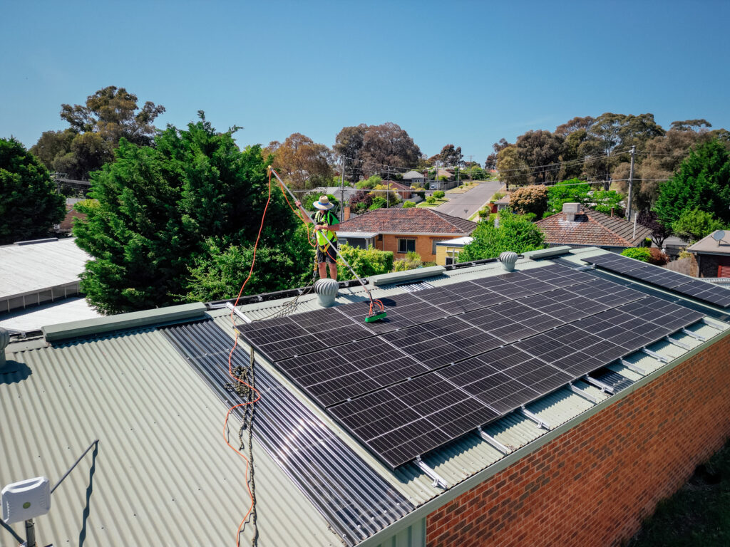 Another photo of a Green Clean Team staff member in safety gear cleaning solar panels on a roof in Bendigo Central Victoria