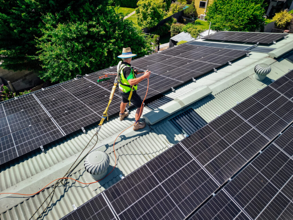 Technician wearing safety gear cleaning solar panels on a rooftop in Central Victoria