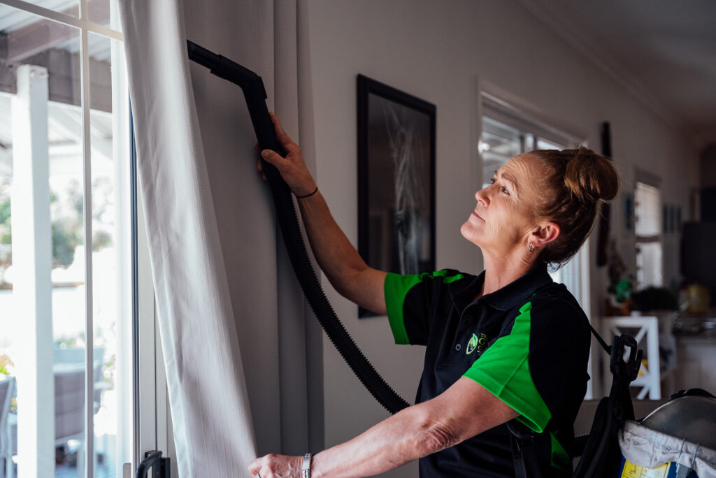 Eco-friendly home cleaning service in Bendigo with a Green Clean Team staff member vacuuming curtains