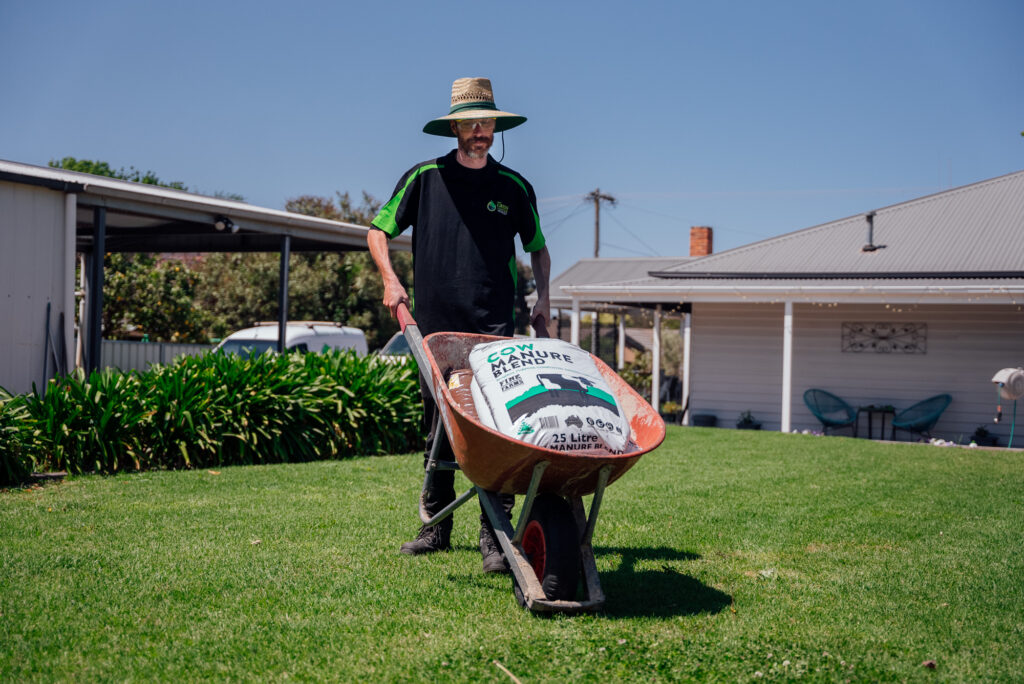 a Green Clean Team member pushing a wheelbarrow on grass during an eco-friendly gardening service in Bendigo