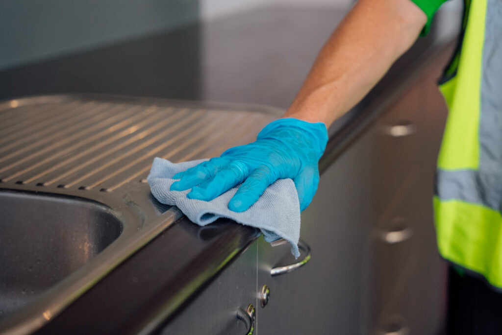 A gloved hand wiping a surface with a blue cloth.