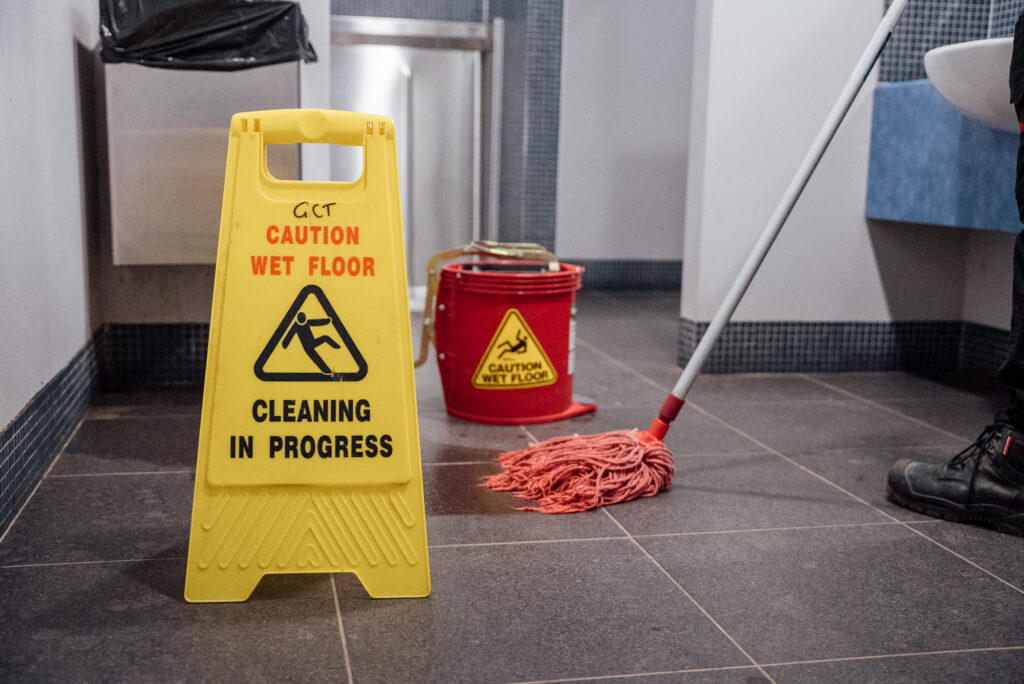 A yellow cleaning in process sign with a mop in the background. A Green Clean Team staff member, who isn't in the shot, is holding the mop as they complete an eco-friendly cleaning service in Central Victoria.