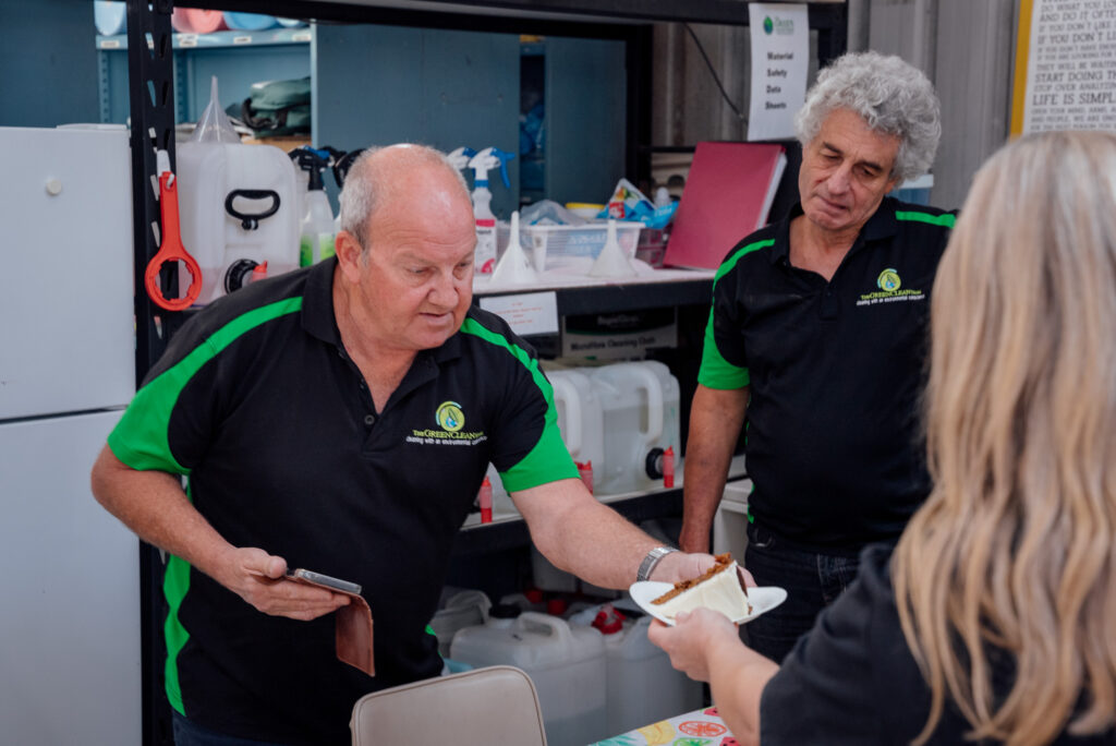 Green Clean Team staff in branded uniforms sharing cake with a client at an event in Bendigo